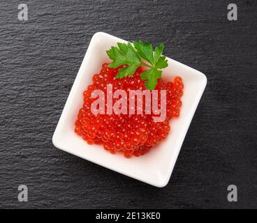 caviar de saumon kéta rouge à grain frais dans un bol en céramique blanche sur fond de pierre d'ardoise noire, vue du dessus Banque D'Images