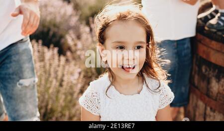 Charmante petite fille caucasienne se posant à l'extérieur dans un champ à proximité ses parents dans une robe blanche passant la fête de la mère ensemble Banque D'Images