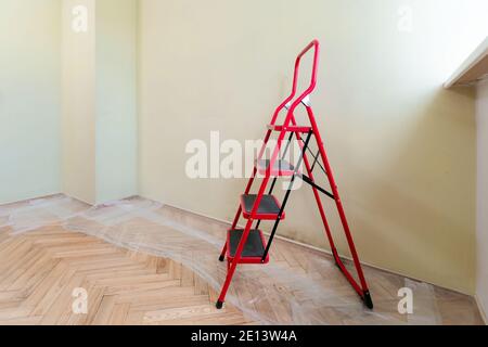 Vider la pièce avec une échelle avant de peindre les murs. Protection en cellophane sur parquet. Rénovation de la maison. Personne Banque D'Images