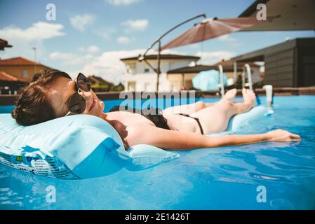 Jeune femme en bikini sur matelas flottant dans la piscine ronde au-dessus du sol. Banque D'Images