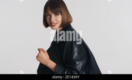 Jolie fille positive brune vêtue dans une tenue décontractée heureux de regarder dans l'appareil photo et souriant isolé sur fond blanc Banque D'Images