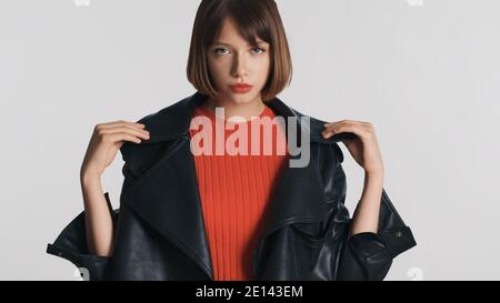 Belle fille brunette avec des cheveux de bob et des lèvres rouges vêtues dans une veste en cuir posé sur l'appareil photo sur fond blanc Banque D'Images