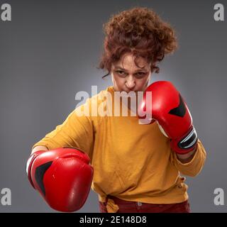 Femme âgée essayant de boxe avec des gants rouges, isolée sur fond gris Banque D'Images