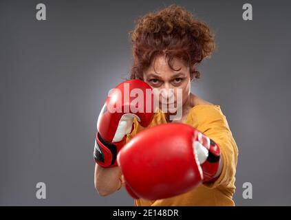 Femme âgée essayant de boxe avec des gants rouges, isolée sur fond gris Banque D'Images