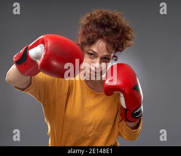 Femme âgée essayant de boxe avec des gants rouges, isolée sur fond gris Banque D'Images