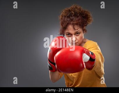 Femme âgée essayant de boxe avec des gants rouges, isolée sur fond gris Banque D'Images