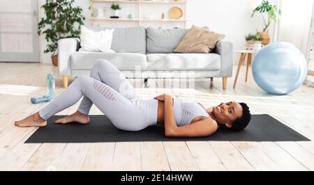 Femme noire millénaire se reposant après avoir fait de l'activité, allongé sur un tapis de yoga à la maison Banque D'Images