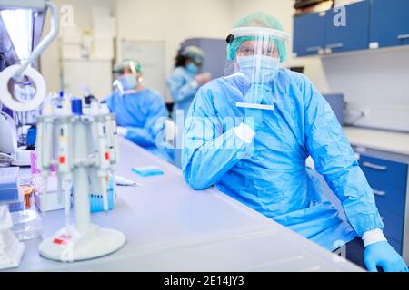 Chercheur en vêtements de protection en laboratoire de biotechnologie avec équipe médicale en arrière-plan Banque D'Images