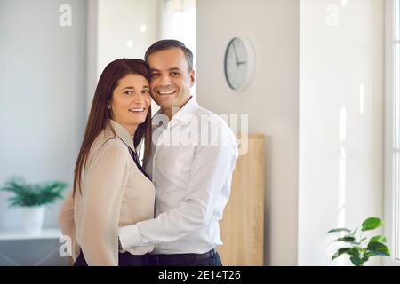 Couple heureux se tenant les uns les autres et regardant la caméra debout dans le bureau de l'entreprise Banque D'Images