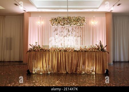 table festive pour les mariés décorée de tissu doré, de fleurs blanches et roses et de bougies. jour de mariage. Banque D'Images