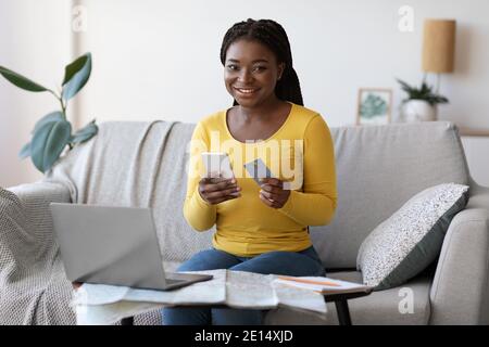 Black Woman Booking Billets en ligne avec smartphone et carte de crédit À la maison Banque D'Images