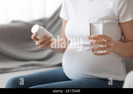 Vitamines prénatales. Femme enceinte tenant un pot avec des suppléments et un verre d'eau Banque D'Images