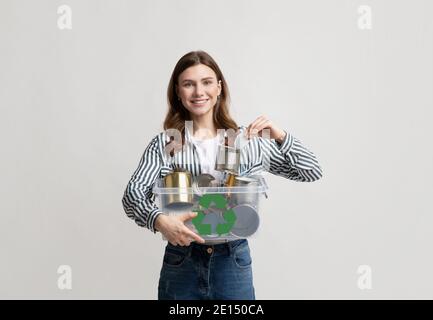 Recyclage des métaux. Jeune femme souriante tenant une boîte en plastique contenant des boîtes en étain Banque D'Images