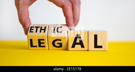 Symbole éthique ou juridique. La main d'homme d'affaires tourne des cubes en bois et change le mot « légal » en « éthique » sur une belle table jaune, fond blanc. Banque D'Images
