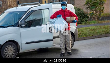 Hampshire, Angleterre, Royaume-Uni. 2020, un messager masculin livrant des colis et des colis pendant l'épidémie de Covid-19 portant des gants et un masque. Banque D'Images