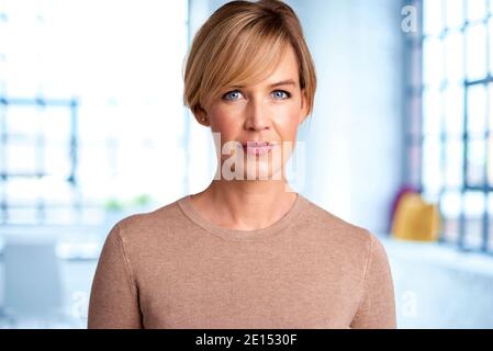 Portrait d'une belle femme blonde aux cheveux regardant l'appareil photo tout en se tenant dans le salon à la maison. Banque D'Images