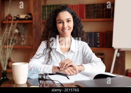 Femme souriante et confiante posant et assise au bureau Banque D'Images