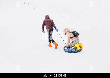 Ski en hiver dans les montagnes en tubing - a l'homme tire un traîneau avec une femme sur un couvert de neige pente Banque D'Images