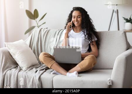 Bonne jeune femme travaillant à la maison, utilisant un ordinateur portable et un smartphone Banque D'Images