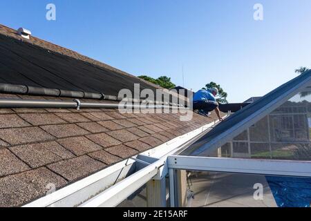 Un vieil homme sur le toit inspecte les gouttières sur la véranda Banque D'Images