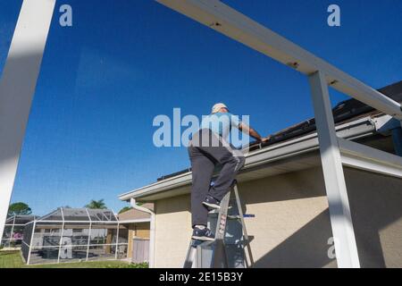 un homme de 60 ans monte sur l'échelle pour se lever Toit de la maison de Floride Banque D'Images