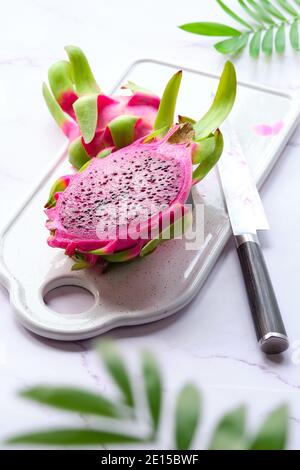 Fruit de dragon rose, pitaya ou pitahaya coupé en cubes sur plaque blanche. Ingrédient de superalimentation sain. Table blanche avec planche à découper, couteau et naturel Banque D'Images