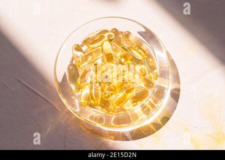 Capsules d'huile de poisson de foie de morue dans un bol en verre sur rose Banque D'Images