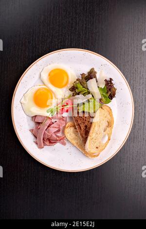 Œufs frits avec tomates, jambon et toasts de ciabatta, sur fond sombre. Petit déjeuner Banque D'Images