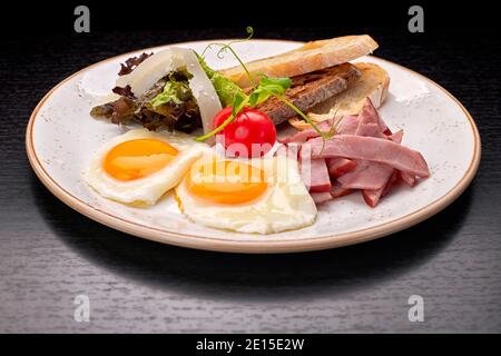 Œufs frits avec tomates, jambon et toasts de ciabatta, sur fond sombre. Petit déjeuner Banque D'Images