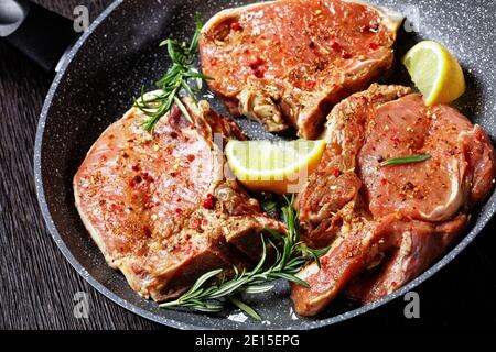 gros plan de côtelettes de porc épicées crues avec des brins de romarin dans une poêle sur une table en bois, vue horizontale d'en haut Banque D'Images