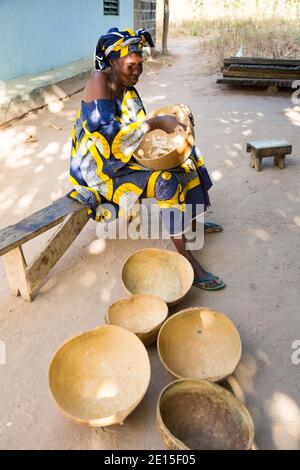 Dame gambienne assise sur un banc simple sur le point de servir de la nourriture dans des bols faits à partir de gourdes dans le village de n'Djemban en Gambie, Afrique de l'Ouest Banque D'Images