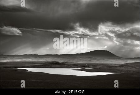 Écosse, Île de Lewis et Harris : approche de nuages de tempête avec des rayons du soleil et des réflexions sur un petit lac Banque D'Images