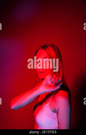 Jeune femme sérieuse et mince regardant l'appareil photo dans la lumière rouge Banque D'Images