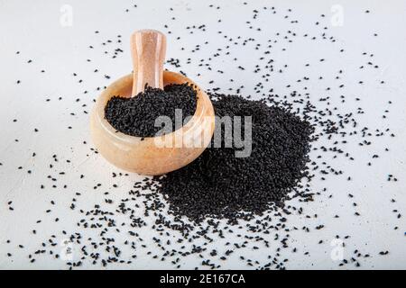 Graines de Nigella sativa également connu sous le nom de cumin noir, kalo jeera, kalonji et carvi noir dans la pelle en fer et le mortier sur fond blanc en bois avec copie sp Banque D'Images