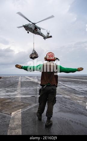 Océan Indien, États-Unis. 04e janvier 2021. L'Airman de la Marine américaine Daniel Williams signale à un hélicoptère MH-60S Sea Hawk qu'il est dégagé lors d'une reconstitution verticale en mer sur le pont de vol du porte-avions de la classe Nimitz USS Nimitz le 4 janvier 2021 dans l'océan Indien. Le Nimitz devait retourner au port d'origine, mais il a été maintenu en place près de l'Iran en raison de tensions accrues. Credit: Planetpix/Alamy Live News Banque D'Images