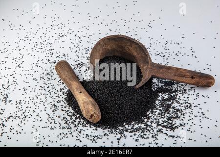 Graines de Nigella sativa également connu sous le nom de cumin noir, kalo jeera, kalonji et carvi noir dans la pelle en fer et le mortier sur fond blanc en bois avec copie sp Banque D'Images