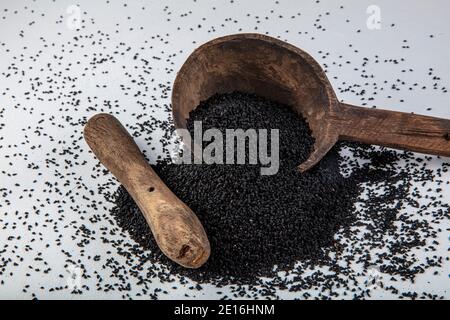 Graines de Nigella sativa également connu sous le nom de cumin noir, kalo jeera, kalonji et carvi noir dans la pelle en fer et le mortier sur fond blanc en bois avec copie sp Banque D'Images