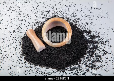 Graines de Nigella sativa également connu sous le nom de cumin noir, kalo jeera, kalonji et carvi noir dans la pelle en fer et le mortier sur fond blanc en bois avec copie sp Banque D'Images