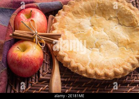 Petite tarte aux pommes maison. Fraîche de la tarte aux pommes au four entourée de pommes et de bâtons de cannelle avec une cuillère à servir en bois. Banque D'Images