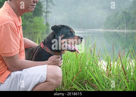 Portrait d'un chien et d'un homme du chiot rottweiler, vue latérale. Nature et fond de lac. Banque D'Images