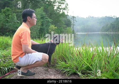 Chien faisant face au lac brumeux avec homme adulte dans une forêt. Concept de loisirs de plein air. Banque D'Images