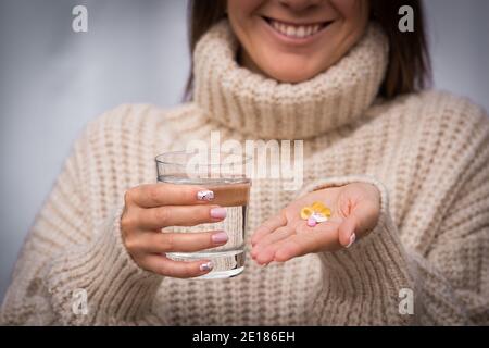 Jeune belle femme souriante tenant des multivitamines et des suppléments et un verre d'eau. Vitamines K2, D, E, A et capsules d'huile de poisson. Banque D'Images