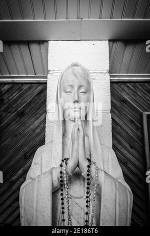 La Vierge Marie. Statue de la Vierge Marie priant avec des perles rosaires dans ses mains. Noir et blanc en orientation verticale. Banque D'Images