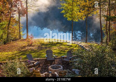 La brume s'élève d'un lac de montagne tandis que le soleil levant illumine le feuillage d'automne entourant une maison de lac haut de gamme en bois rond dans les montagnes de la Géorgie du Nord. Banque D'Images