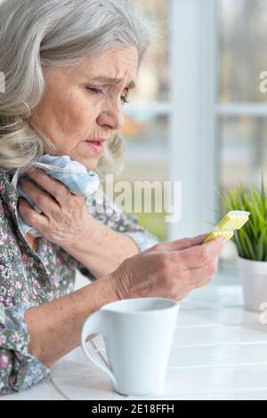 Sick senior woman sitting at table at home avec mal de gorge Banque D'Images
