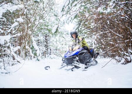 Homme en motoneige en montagne d'hiver. Motoneige. Homme conduisant une motoneige dans une forêt enneigée Banque D'Images