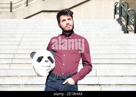 Jeune homme d'affaires avec un masque de tête de panda dans ses mains, debout sur les escaliers. Homme d'affaires bizarre. Banque D'Images