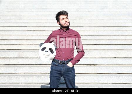 Jeune homme d'affaires avec un masque de tête de panda dans ses mains, debout sur les escaliers. Homme d'affaires bizarre. Banque D'Images