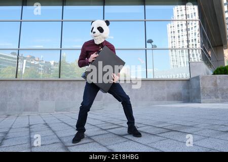 Un voleur de sexe masculin portant un masque de tête de panda dérobe un porte-documents s'échappant et regardant en arrière. Voleur bizarre. Banque D'Images