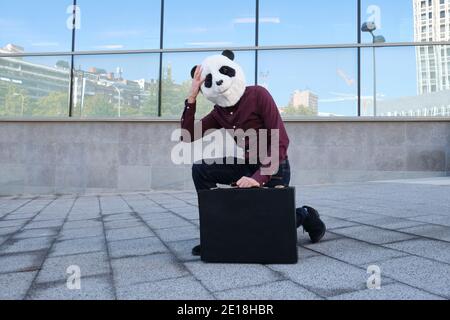 Un voleur de sexe masculin portant un masque de tête panda dérobant un porte-documents fatigué de courir. Voleur bizarre. Banque D'Images